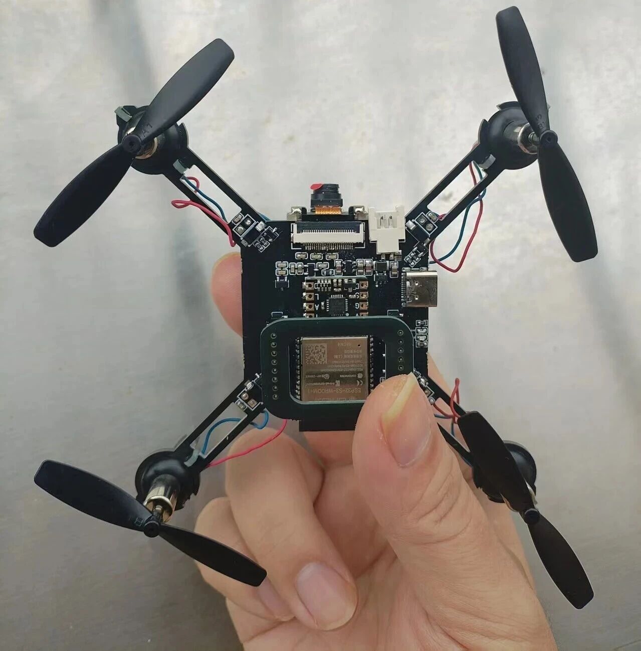 ESP32-S3 micro drone resting in a hand, showing PCB, motors and propellers